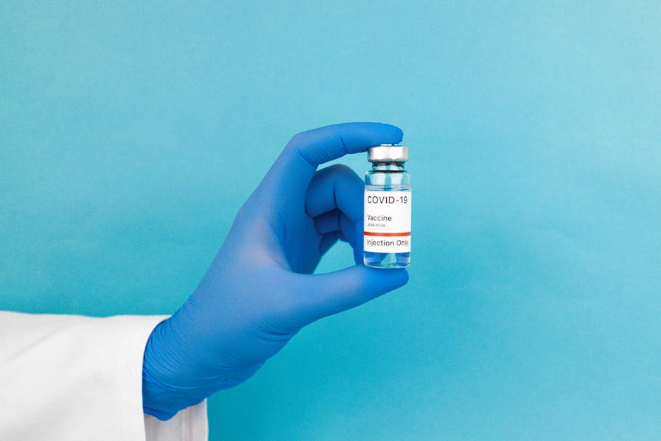 Close-up of a gloved hand holding a COVID-19 vaccine vial against blue background.