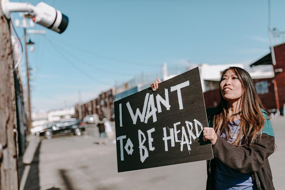 A woman holds a sign reading 'I want to be heard' during a protest on a sunny city street.